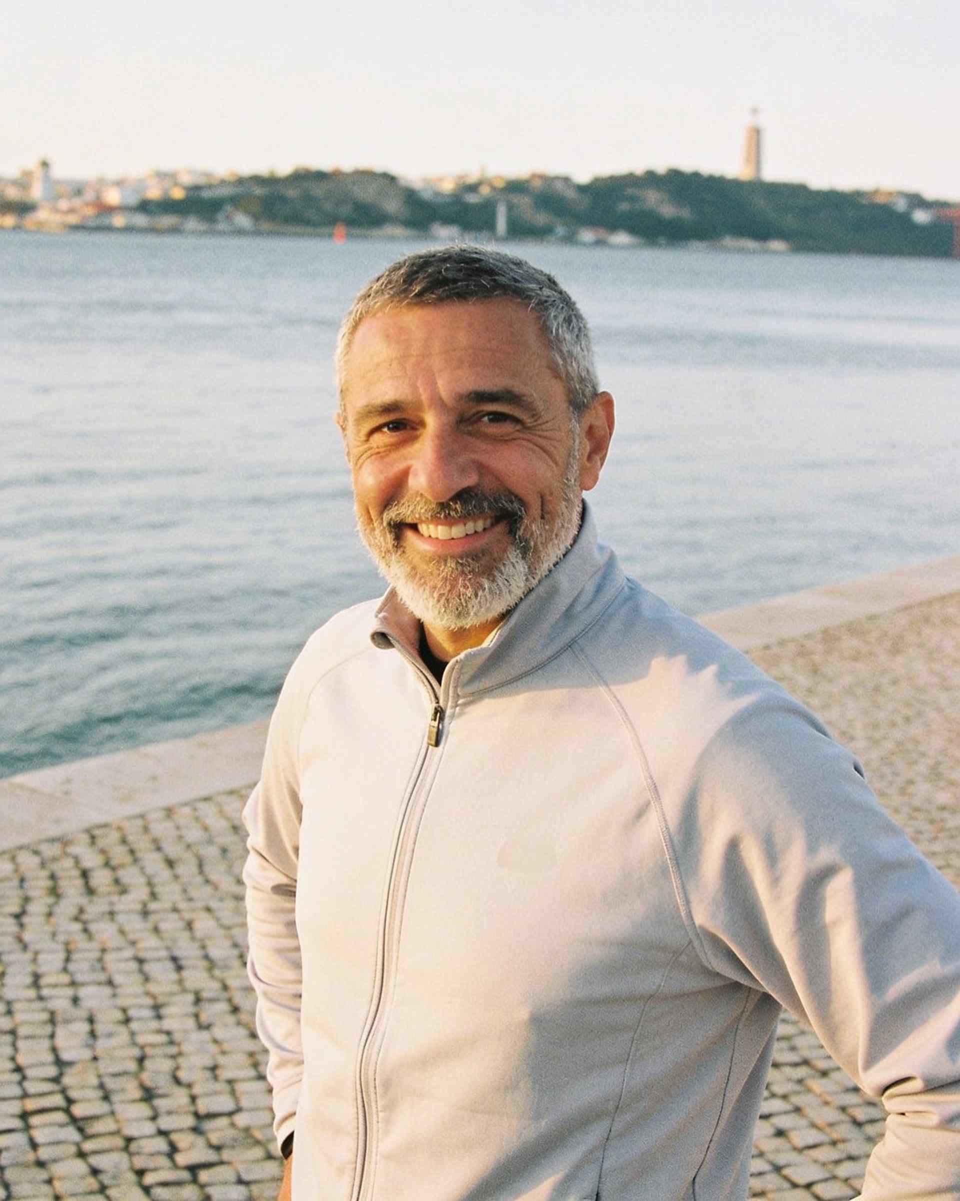 A man in his fifties with a grey beard in a running jacket by a river
