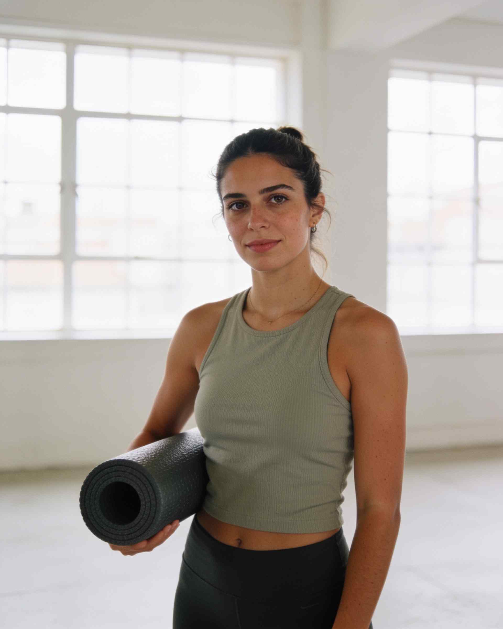 A young woman in sports clothes holding a foam roller in a bright studio